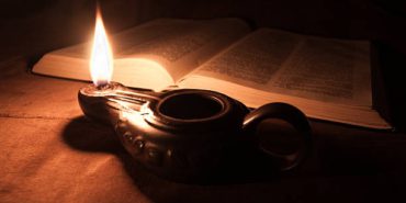 Close-up of an oil lamp and an opened Bible.